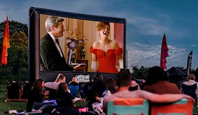 Pretty Woman plays on a large outdoor cinema screen at dusk whilst people watch in front.