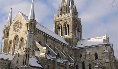 Chichester Cathedral with snow on the groud. Sunlight on the cathedral and a blue sky with clouds.