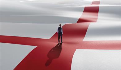 A small figure of a man stands with his back to the camera in the centre of a giant Cross of St George - the England football team's flag. The figure