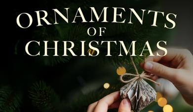 A hand hanging up an origami Christmas ornament made of music manuscript on a tree.