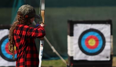 Child lining up shot in front of archery target.