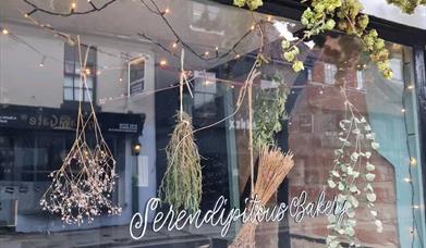 A view of Serendipitous bakery from outside with hops and plants hanging in the window